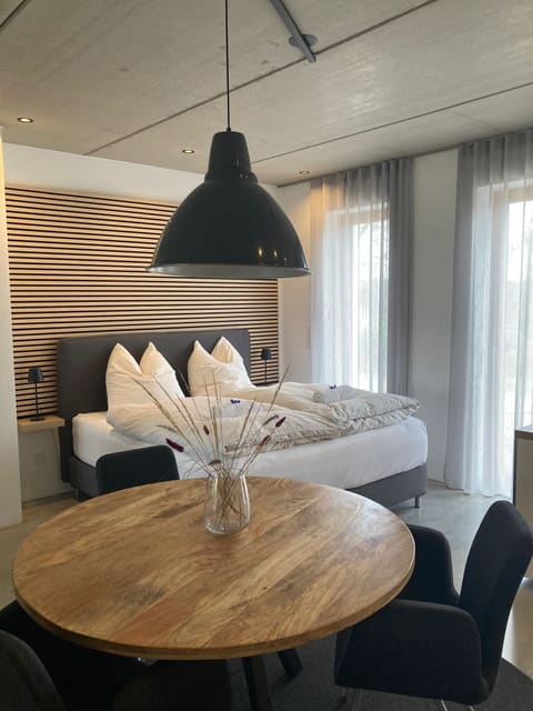 Studio im Grünen: Esstisch aus Holz vor dem Boxspringbett mit Holzwand